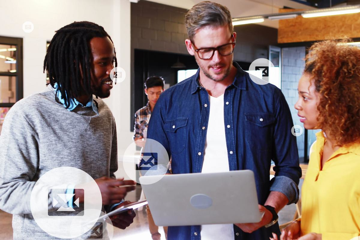 Three coworkers reviewing email together on a laptop in a modern office, with floating email icons.